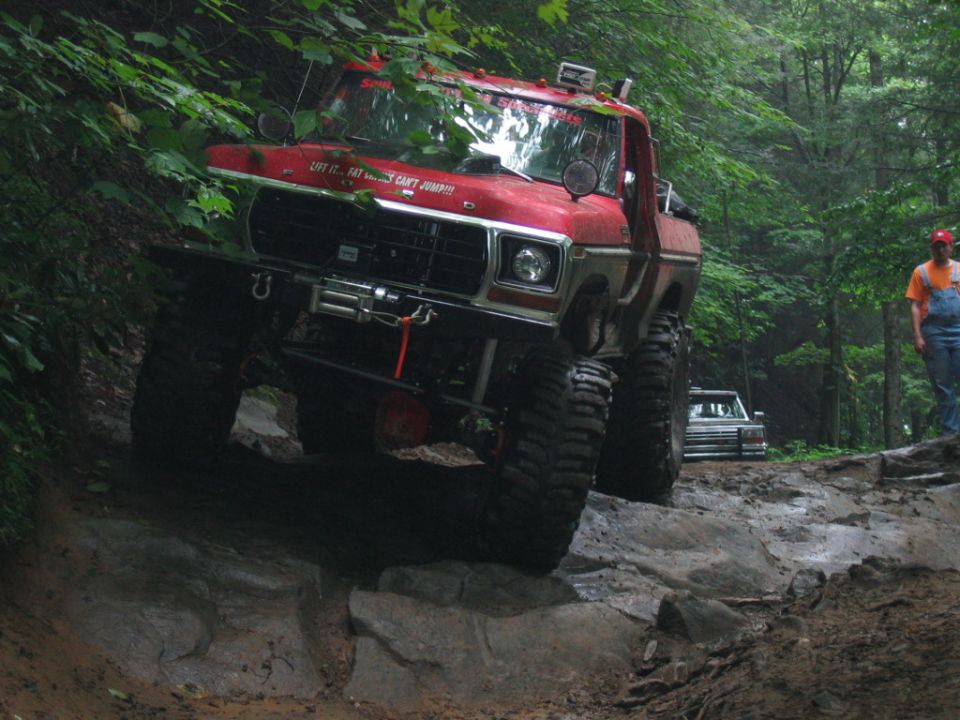 Red 1979 Ford F-Series pickup truck off-roading on a rocky, wooded trail