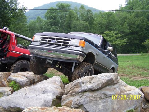 1979 Ford F-150 - A gray and black Ford Bronco navigates a rocky obstacle course, with a red off-road vehicle visible to the left.