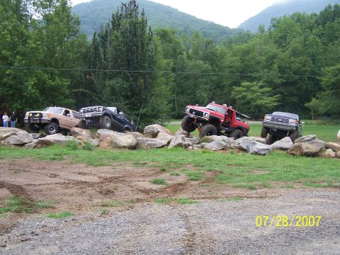 1979 Ford F-150 - Several trucks are shown off-roading over a rocky terrain with trees and mountains in the background.