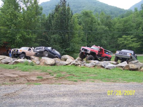 1979 Ford F-150 - Modified trucks traverse a challenging rock obstacle course on a sunny day.
