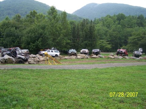 1979 Ford F-150 - Multiple off-road vehicles are parked on a rocky terrain with a backdrop of trees and mountains.