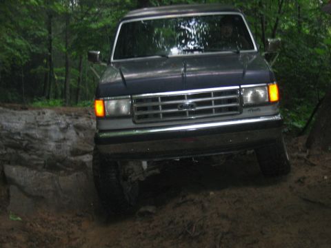 1992 Ford Mustang - A dark blue Ford Bronco navigates a challenging muddy terrain.