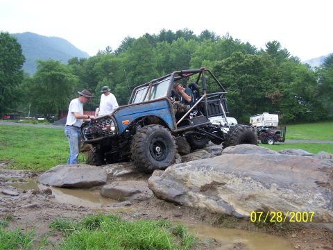 1979 Ford F-150 - Modified off-road vehicle attempts to traverse a rocky, muddy terrain with assistance from bystanders.