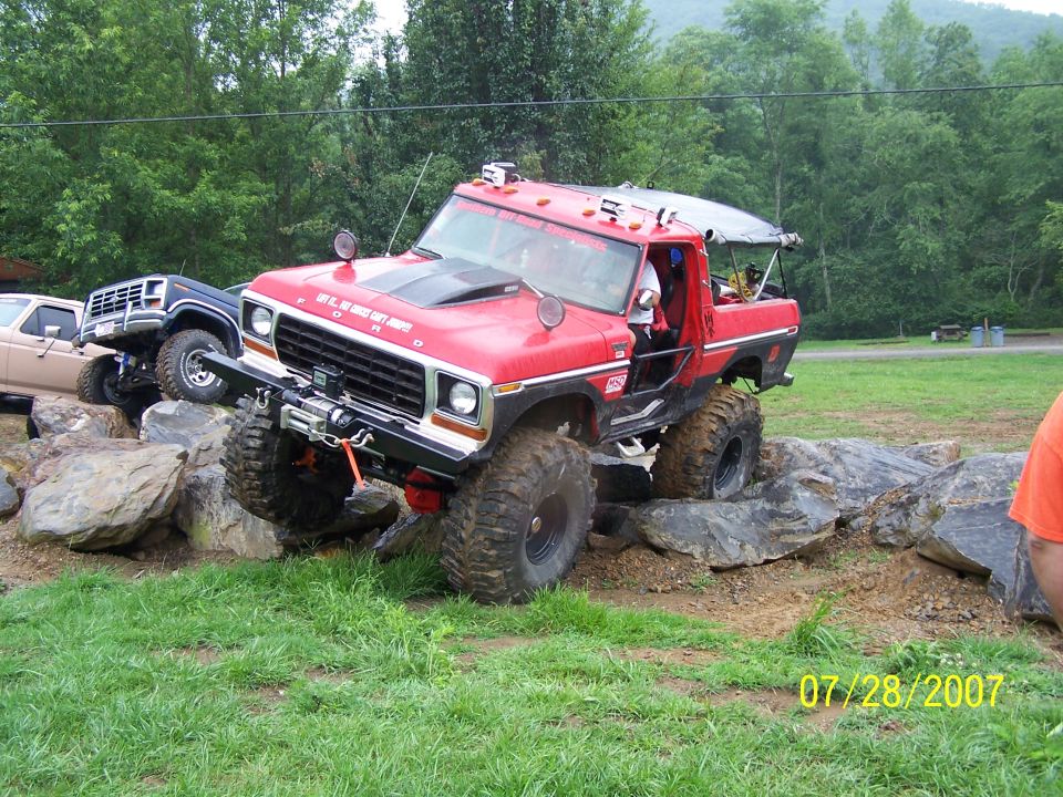 Red lifted Ford pickup truck navigating rocks, with a black Ford Bronco and a tan pickup in the background. Date stamp reads 07/28/2007