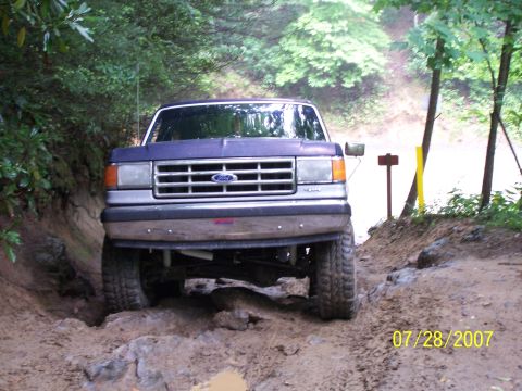 1979 Ford F-150 - A blue Ford truck is seen from the front, driving through a challenging muddy and rocky terrain.