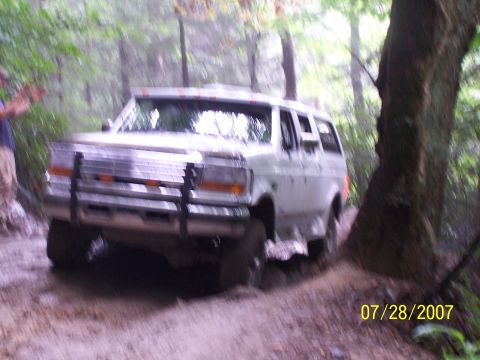 1979 Ford F-150 - A white SUV navigates a muddy forest trail on a hazy day.