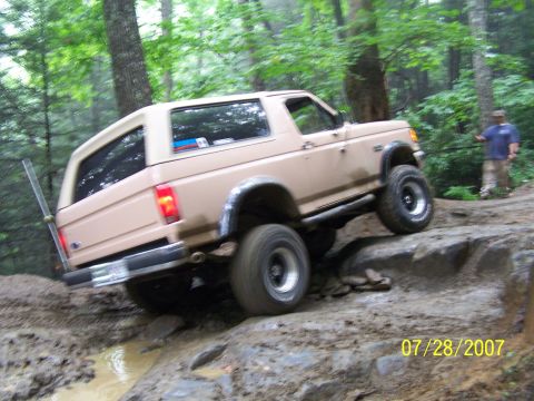 1979 Ford F-150 - A tan Ford Bronco navigates a challenging rocky and muddy off-road trail.