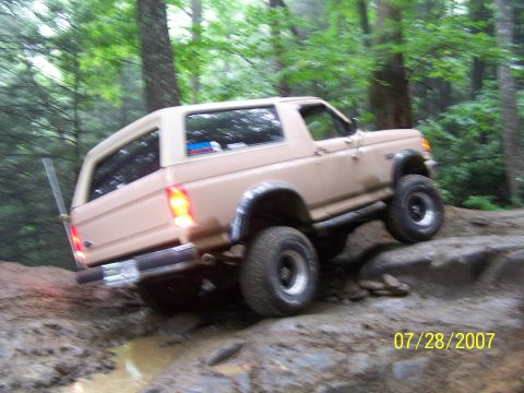 1979 Ford F-150 - A tan SUV tackles a challenging off-road course with steep inclines and muddy terrain.