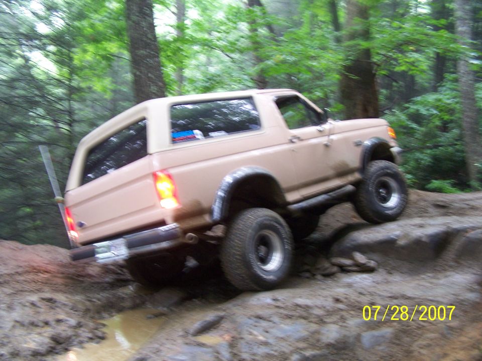 Tan SUV with a removable hardtop navigating a rocky, muddy off-road trail