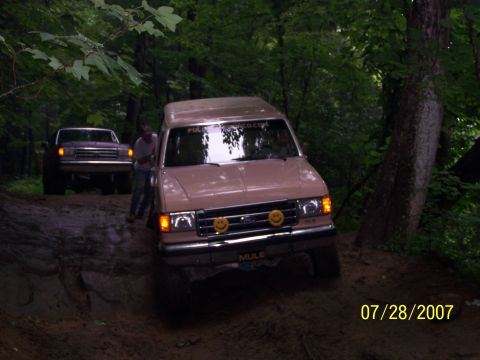 1979 Ford F-150 - A tan van with smiley face lights navigates a muddy off-road trail, with another truck following behind.