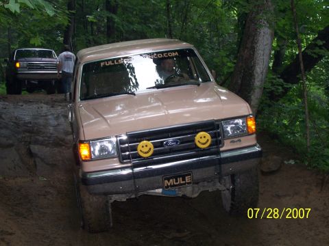 1979 Ford F-150 - Two Ford F-Series trucks navigate a muddy off-road trail in a wooded area.