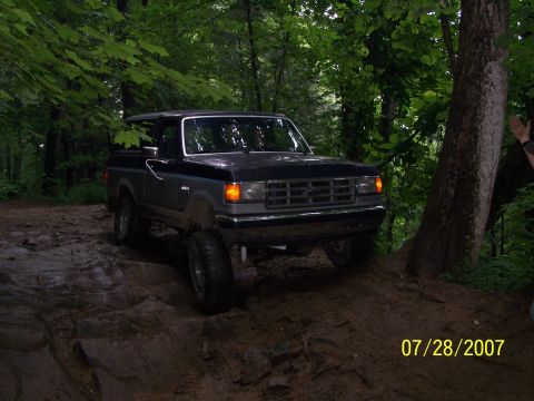1979 Ford F-150 - A Ford Bronco navigates a challenging off-road trail surrounded by trees.