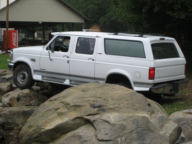 White SUV with a long wheelbase and four doors, driving over rocks