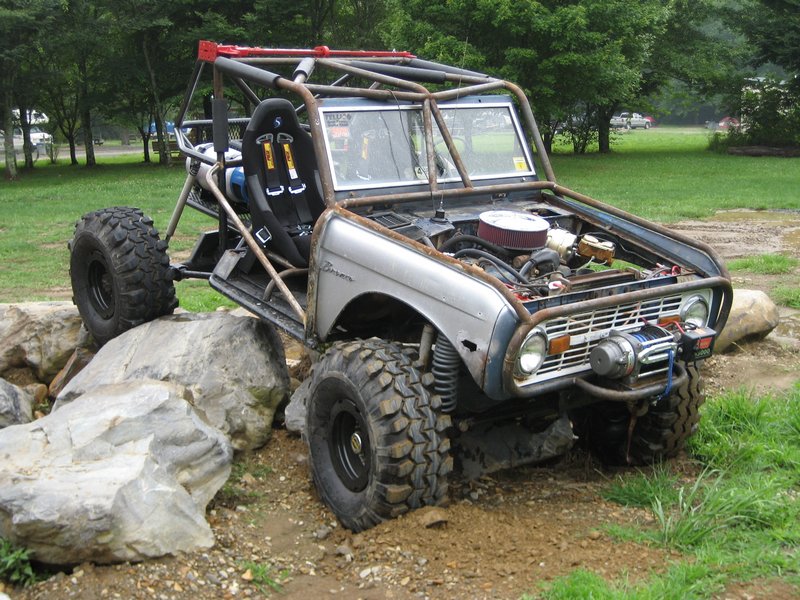 Modified Ford Bronco buggy with roll cage and large tires climbing over rocks