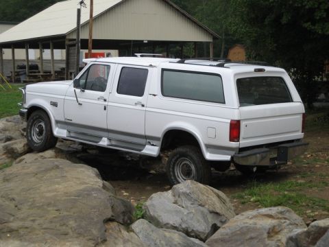 1995 Ford Bronco - White Ford SUV navigates a rocky obstacle course in front of a building.