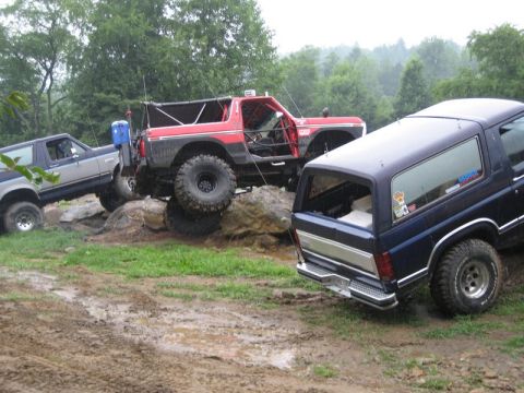 1995 Ford Bronco - Several Ford Broncos navigate a challenging off-road course with muddy ground and large rocks.