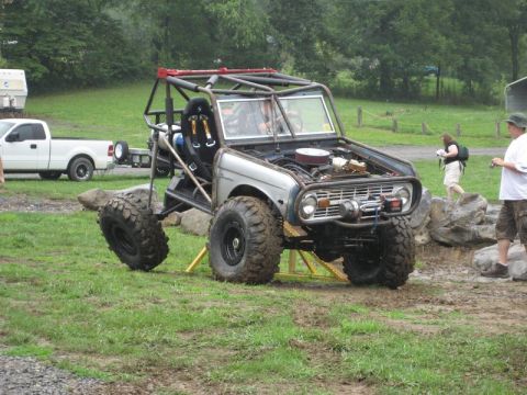 1995 Ford Bronco - A heavily modified SUV with a roll cage and oversized tires is shown outdoors, with a white pickup truck visible in the background.