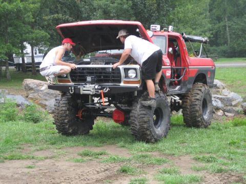 1995 Ford Bronco - Two men inspect the engine of a heavily modified red truck with oversized tires.