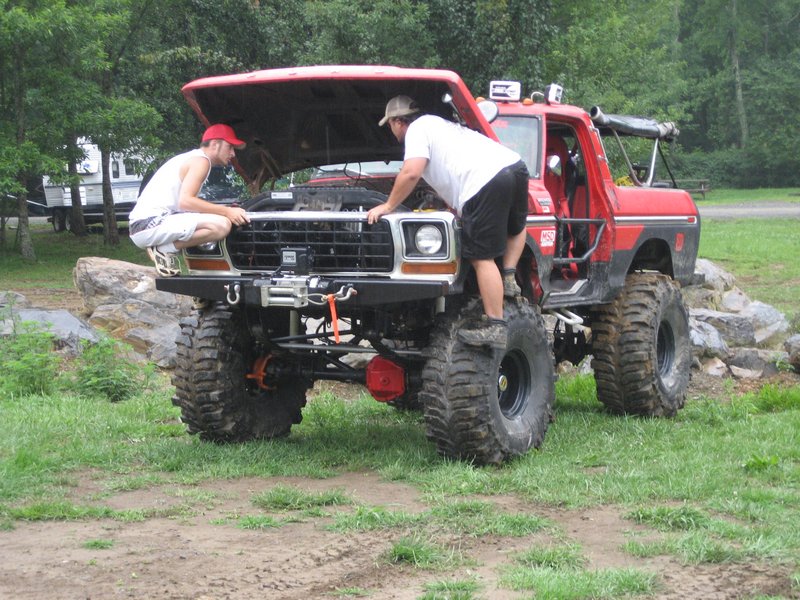 Red lifted truck with large tires and hood open, two men examining the engine bay
