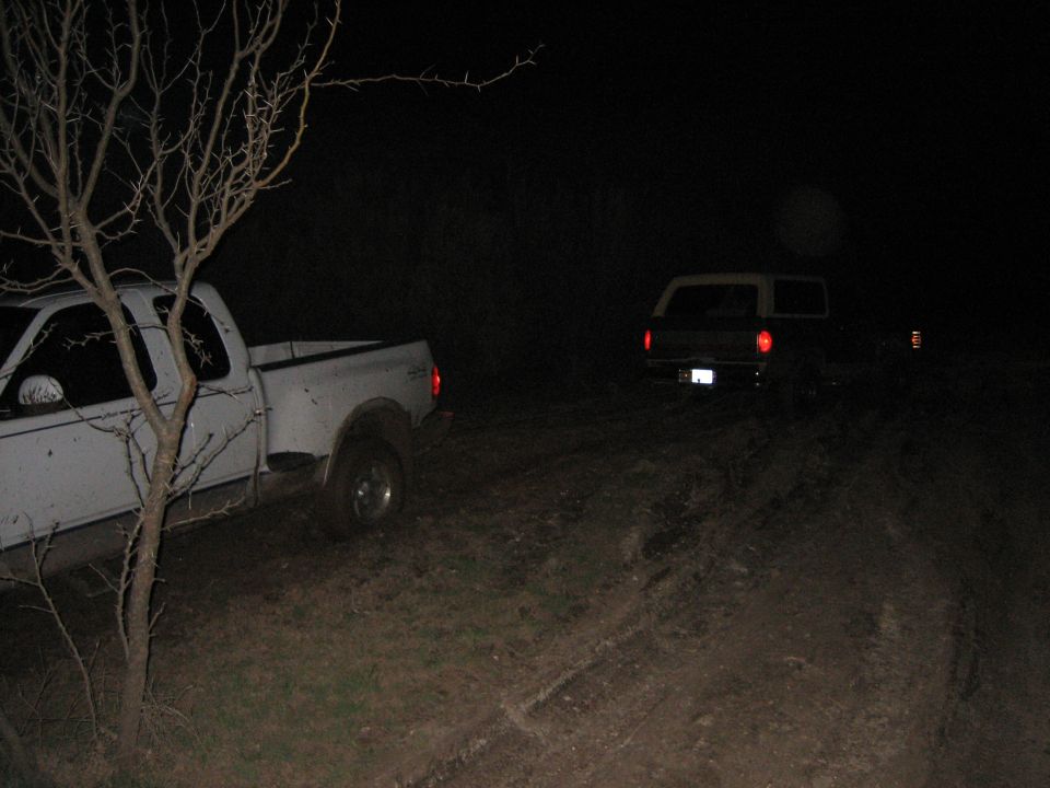 White pickup truck and a dark SUV parked on a dirt road at night