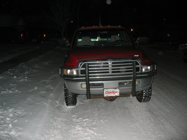 Red Dodge pickup truck with a chrome grille and brush guard, parked in snow