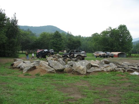 1995 Ford C-350 (Centurion Conversions) - Off-road vehicles tackle a challenging rock obstacle course with a barn and trees in the background.