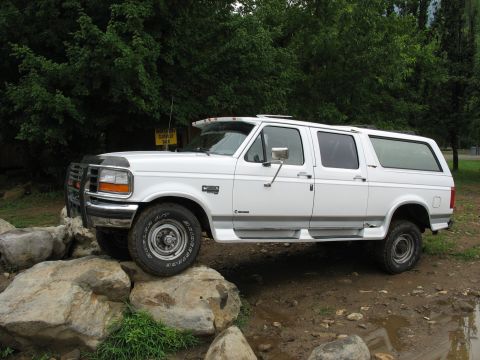 1995 Ford C-350 (Centurion Conversions) - White 1995 Ford C-350 Centurion Conversions extended cab truck with camper shell navigating rocky terrain.