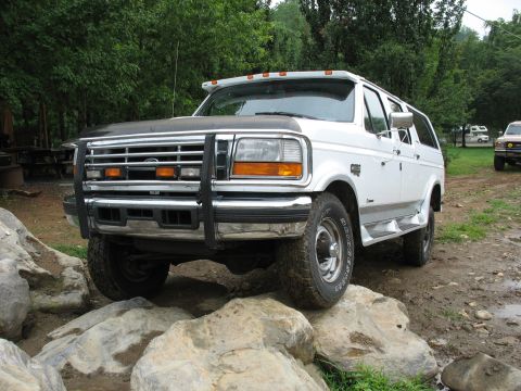 1995 Ford C-350 (Centurion Conversions) - This white SUV is positioned on large rocks, with trees and another vehicle visible in the background.