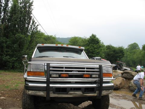 1995 Ford C-350 (Centurion Conversions) - A Ford truck is parked on a muddy trail with other off-road vehicles and people in the background.