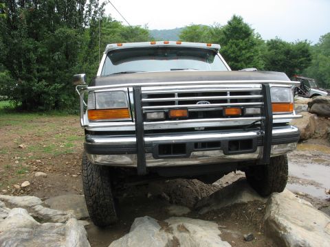 1995 Ford C-350 (Centurion Conversions) - A Ford F-Series truck with a chrome grille guard is shown from the front, driving over rocks.