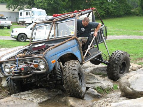 1995 Ford C-350 (Centurion Conversions) - A heavily modified buggy navigates a rocky obstacle course with a driver preparing to take the wheel.