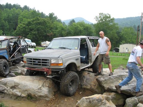 1995 Ford C-350 (Centurion Conversions) - Modified Ford Bronco tackles a rocky obstacle course with a man standing by the open door.