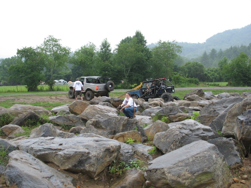 Two off-road vehicles, one a truck and the other a buggy, are parked near a rocky area with people around
