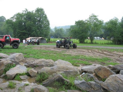 1995 Ford C-350 (Centurion Conversions) - Several off-road vehicles are gathered in a field near a campsite with tents visible.