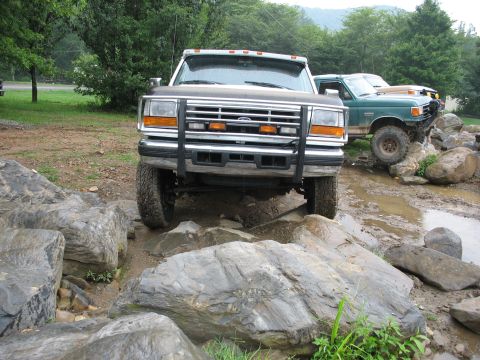 1995 Ford C-350 (Centurion Conversions) - Two trucks navigate a rocky, muddy terrain, with the lead truck positioned directly in front of the camera.