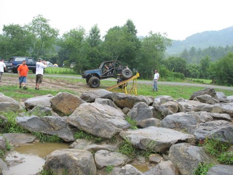 1995 Ford C-350 (Centurion Conversions) - An off-road vehicle is positioned on a ramp as part of an obstacle course, with spectators and another truck nearby.