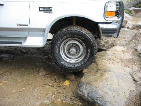 1995 Ford C-350 (Centurion Conversions) - Front wheel of a 1995 Ford C-350 (Centurion Conversions) navigating rocky terrain.