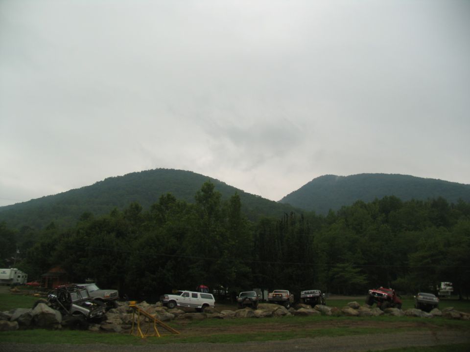 Several off-road vehicles parked on rocky terrain with trees and mountains in the background