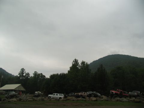 1995 Ford C-350 (Centurion Conversions) - A collection of trucks and SUVs are parked on a rocky area, with trees and a hill forming the backdrop.