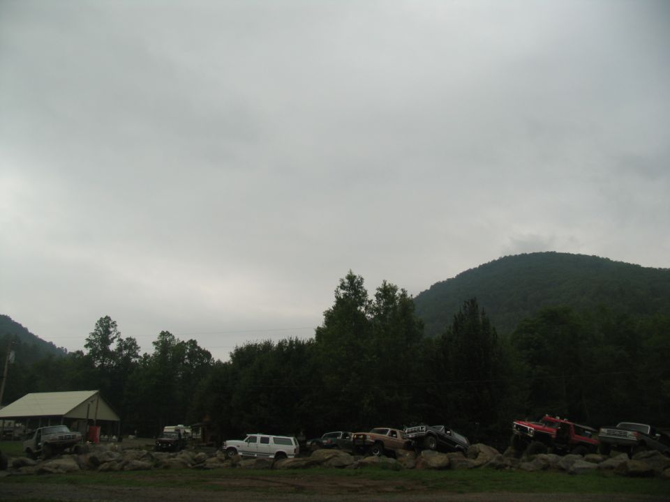 Several trucks and SUVs parked on rocks with trees and a hill in the background