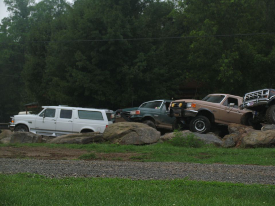 White SUV and tan truck on rocks, side view. The SUV appears to be a 1992 Ford Econoline conversion