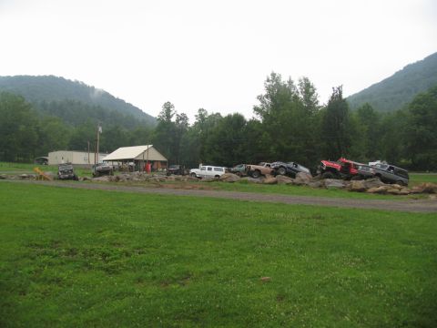 1995 Ford C-350 (Centurion Conversions) - A collection of , lifted vehicles are staged on a rocky terrain with a building and trees in the background.