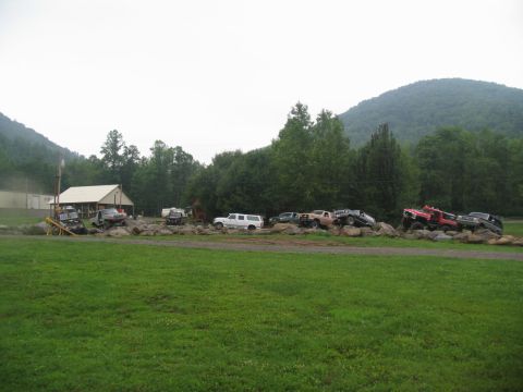 1995 Ford C-350 (Centurion Conversions) - Multiple off-road vehicles navigate a challenging rocky obstacle course near a wooded area.