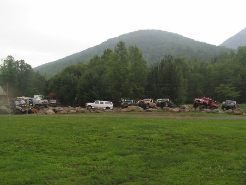 1995 Ford C-350 (Centurion Conversions) - Several modified trucks and SUVs are positioned on a large rock formation, appearing to be part of an off-road event or park.