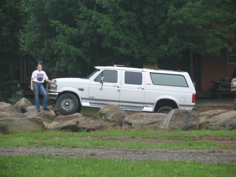 White extended SUV with a woman standing next to it, positioned on large rocks