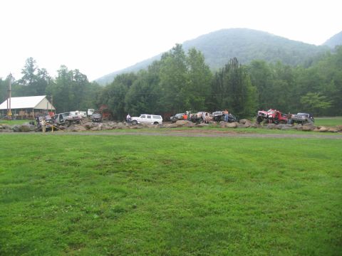 1995 Ford C-350 (Centurion Conversions) - Multiple off-road vehicles are gathered in an outdoor setting with a building and mountainous terrain.