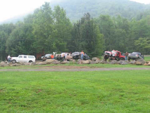 1995 Ford C-350 (Centurion Conversions) - Multiple modified trucks and an SUV navigate a rocky obstacle course in a rural, wooded area.