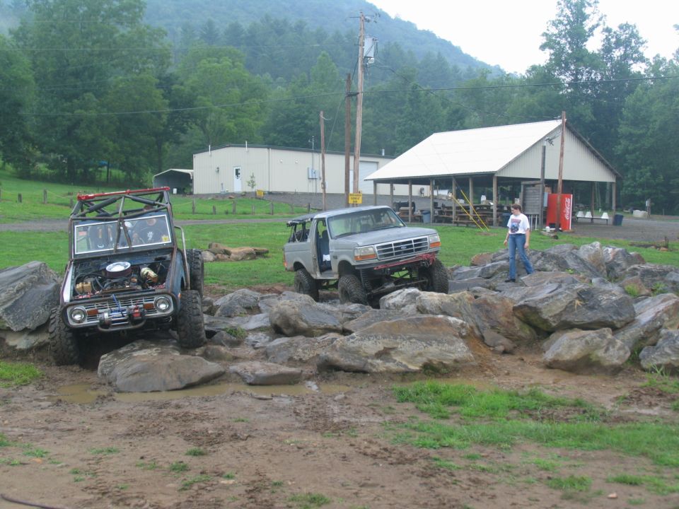 Silver Ford Bronco off-roading over rocks, hood open. Another off-road vehicle in background