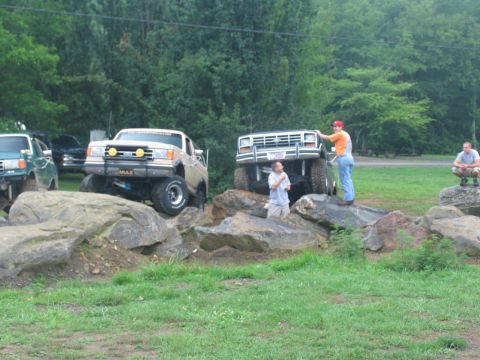 1995 Ford C-350 (Centurion Conversions) - Two lifted trucks navigate a rocky obstacle course with spectators watching.