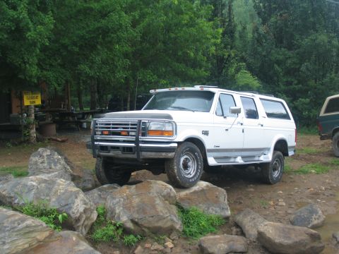1995 Ford C-350 (Centurion Conversions) - A white SUV navigates a rocky terrain with trees in the background.